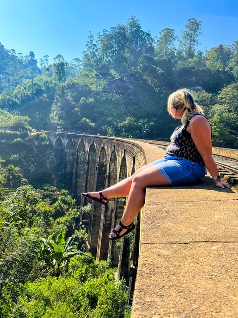 Person sitting on the edge of a railway bridge in a lush green forest.
