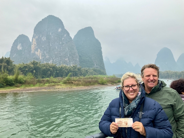       Couple in front of karst mountains reflected in a river, with cloudy skies.
  