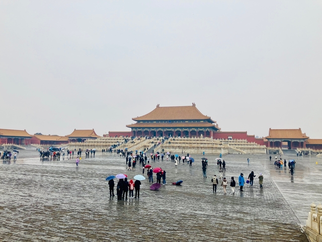 People with umbrellas visiting the vast expanse of the Forbidden City.