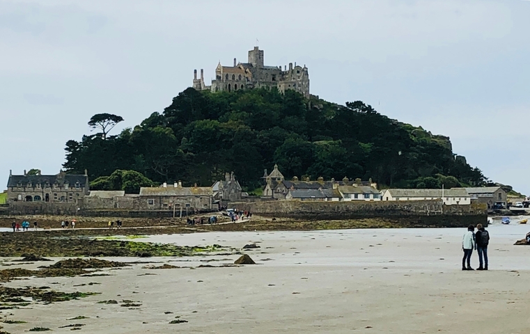 Historic castle on a hill with buildings below, beach in foreground.