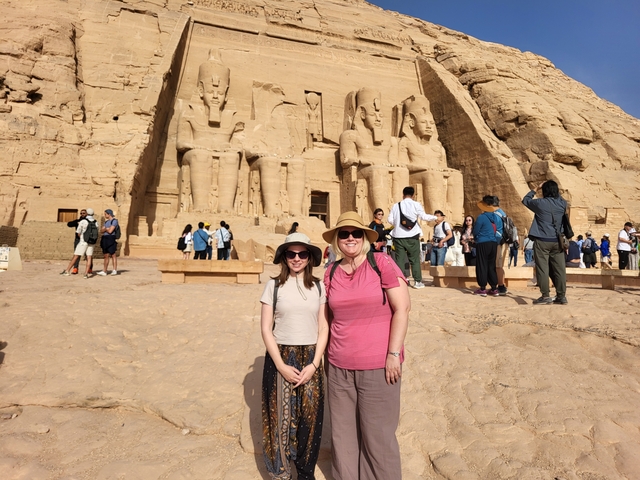 Two women posing in front of a rock temple with large statues.