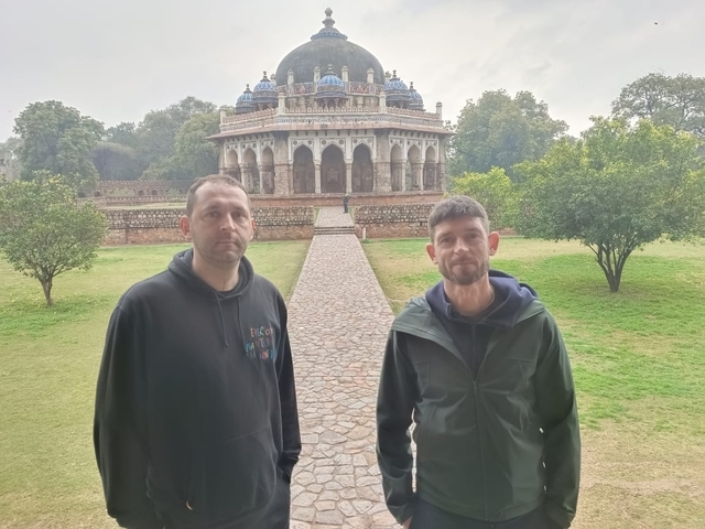 Two men standing in front of a historic dome-shaped structure with a pathway in front.