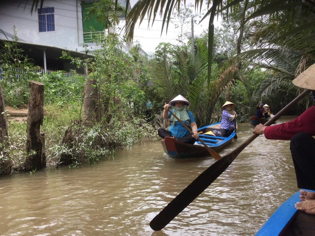       People navigating a narrow river canal in a small boat surrounded by lush vegetation.
  