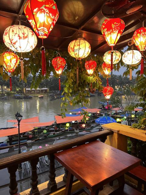       View of a colorful river with lanterns, tables, and chairs
  