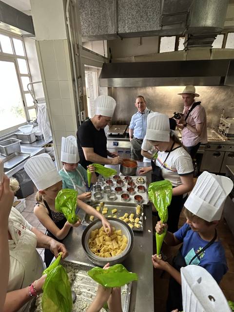       People in a kitchen making pasta with green piping bags.
  