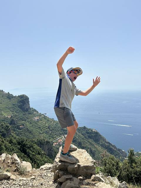       Child playfully posing on rocks with a view of the sea.
  