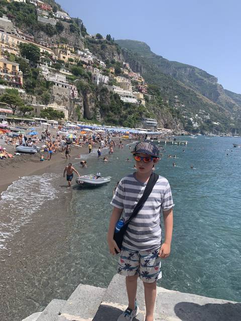       Child posing by the seaside with a busy beach.
  