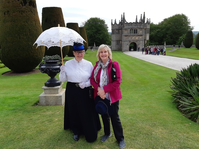 Two women pose in historical costumes in front of an old stone building