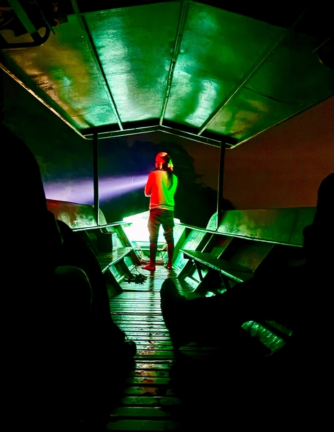 Person standing on a boat at night with a flashlight.