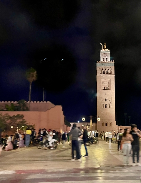       Nighttime view of a lit tower in a traditional Moroccan setting.
  
