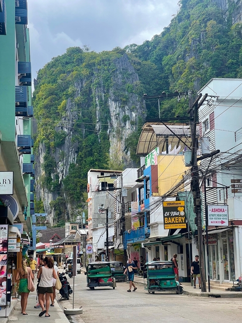Street view of El Nido with signs and cliffs in the background.