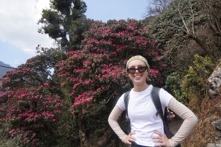       A woman posing with pink flowers on a hiking trail.
  