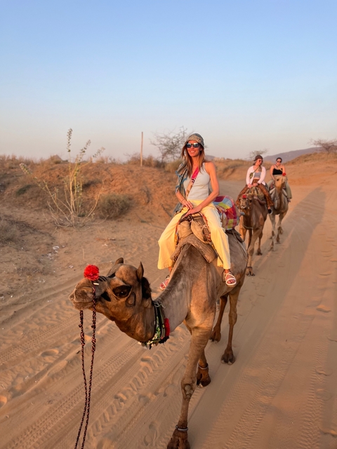       People riding camels in the desert during sunset.
  