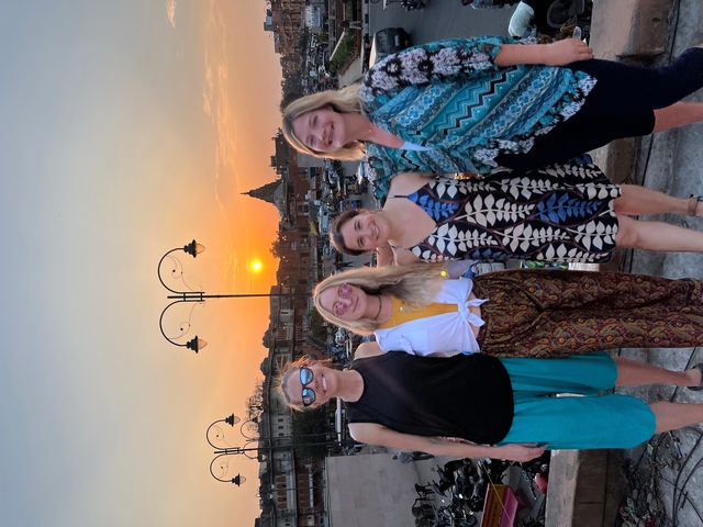       Four women posing on a rooftop with a sunset background.
  