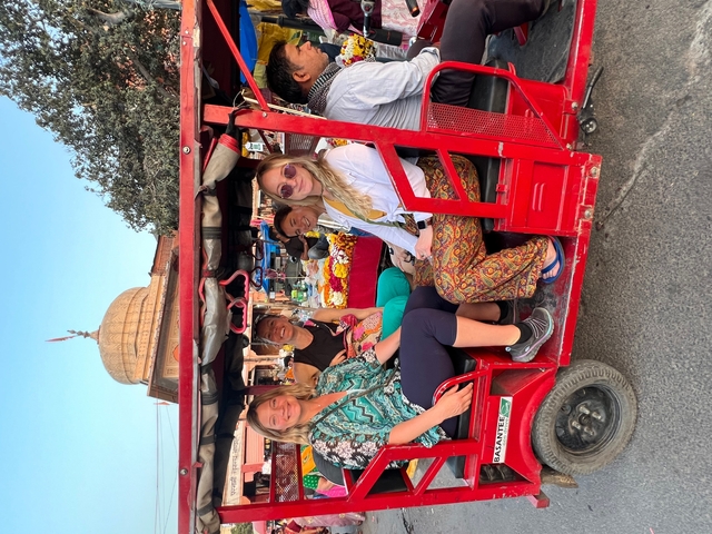       Group of people in a red tuk-tuk on a street.
  