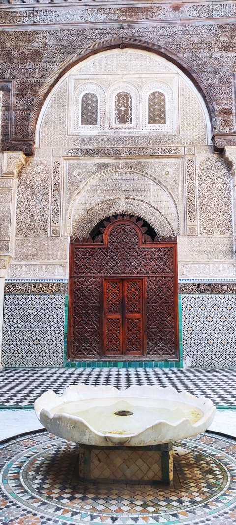Intricate wooden door with detailed carvings surrounded by geometric tile patterns.