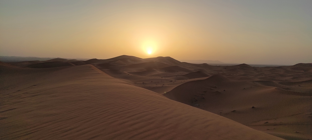 Desert landscape with sand dunes and a setting sun.