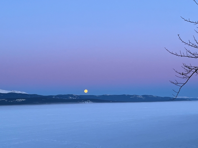 Moonrise over a mountain range with a colorful evening sky.