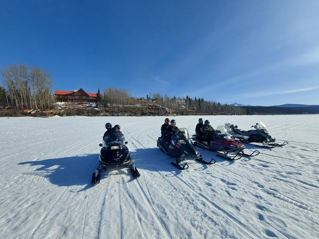 Group of people on snowmobiles in a snowy terrain with cabins.