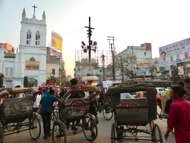       Busy street scene with rickshaws and advertisements.
  