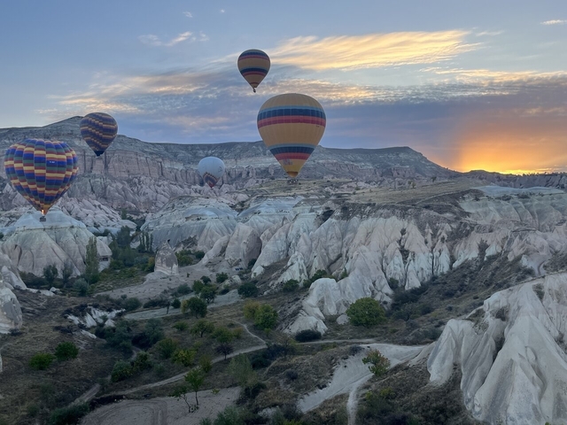 Hot air balloons flying over rocky landscape at sunrise.