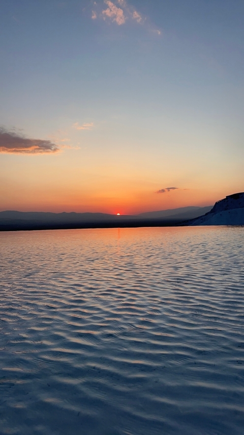 Sunset over calm water with distant mountains.