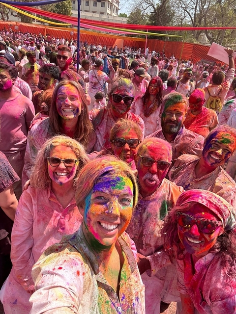       Group of people covered in vibrant colored powders celebrating Holi.
  