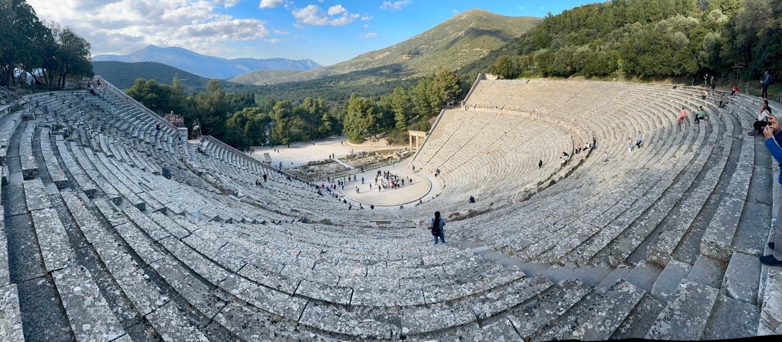 Ancient Greek amphitheater surrounded by lush mountains.