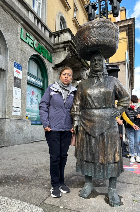       Woman posing with a statue in an urban setting.
  