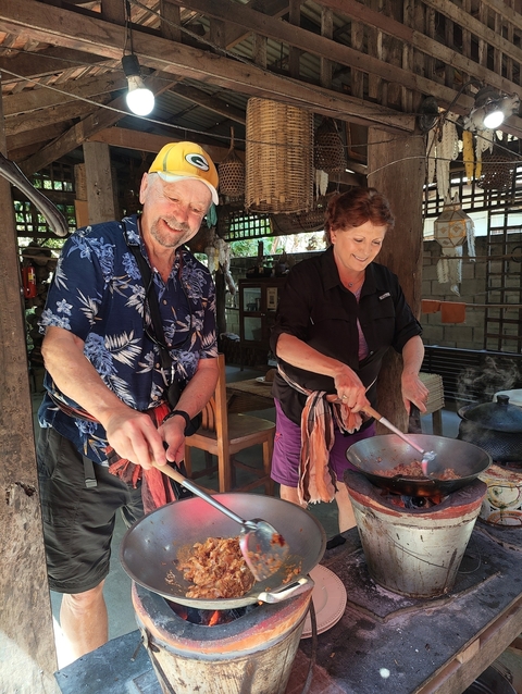       Couple cooking food together at an outdoor venue.
  