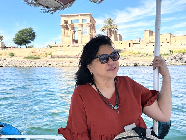 Woman on a boat with Egyptian temple ruins in the background.