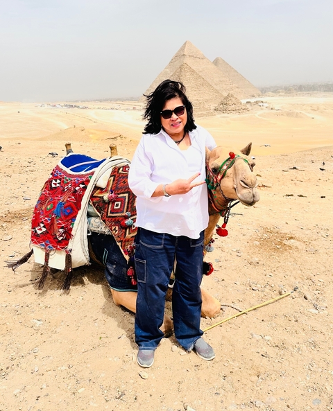 Woman posing with a colorful decorated camel in the desert.
