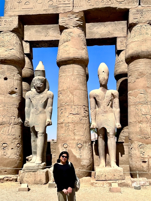 Ancient Egyptian statues and columns under a bright blue sky.