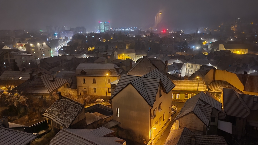 Night view of a cityscape with snow-dusted rooftops and illuminated buildings.