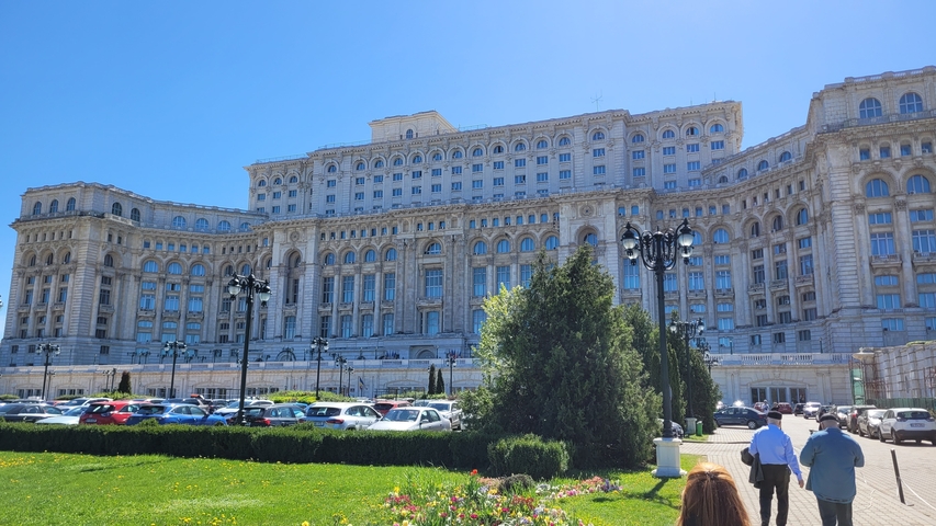       The massive Palace of the Parliament with green gardens below under a bright sky.
  
