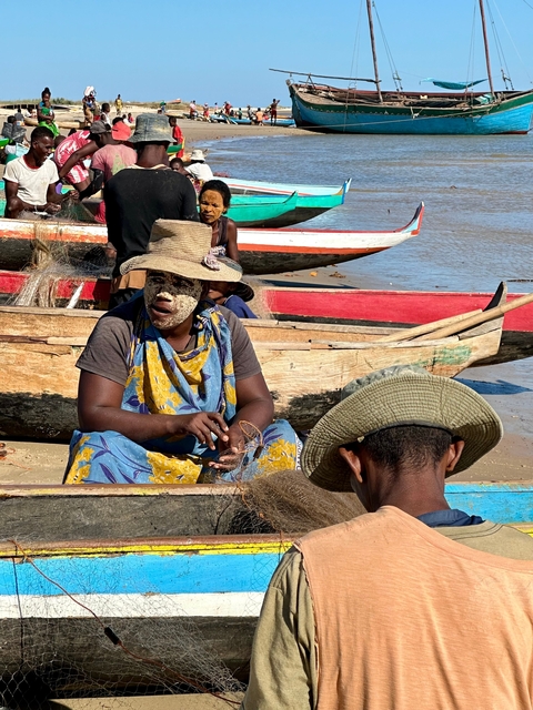       People in traditional attire working with fishing nets near colorful boats.
  