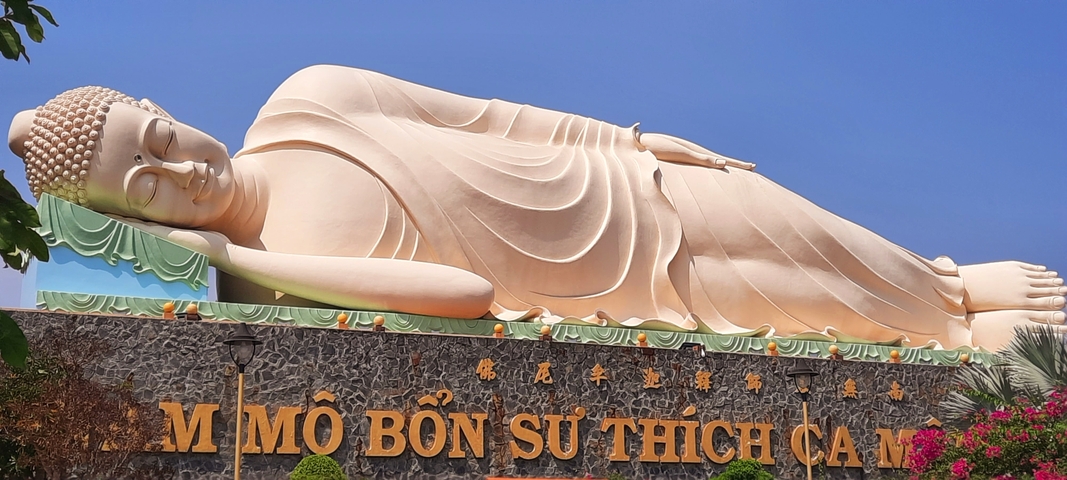       Large reclining Buddha statue under a clear blue sky.
  
