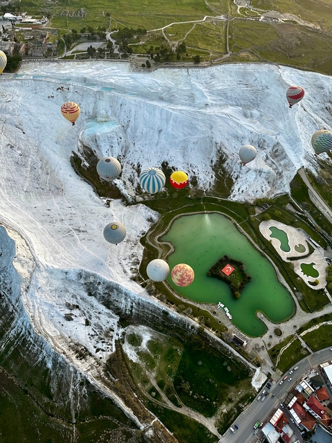 Hot air balloons floating over the white terraces and a green lake
