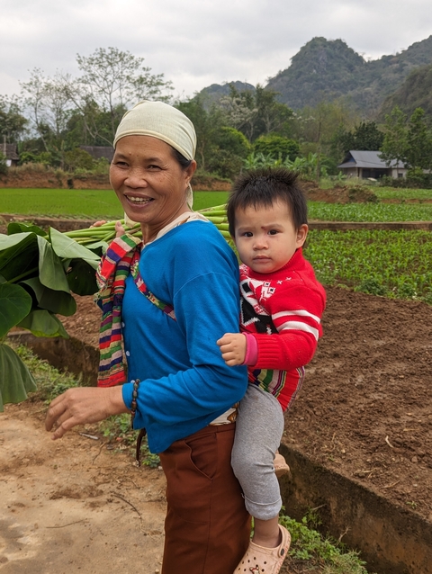 Woman carrying leaves with a young child in the field.