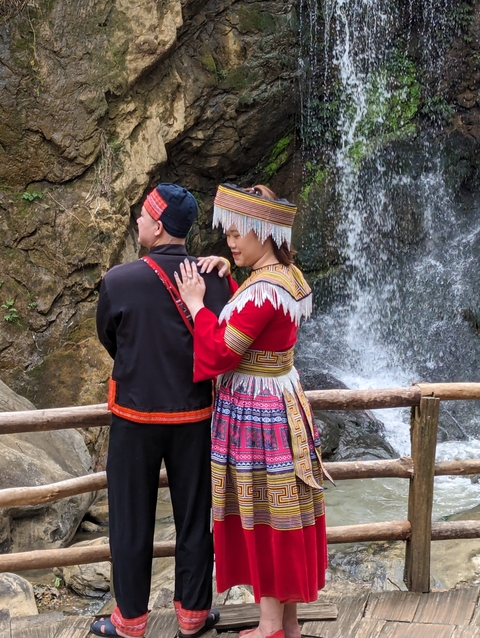 Couple in traditional attire posing in front of a waterfall.