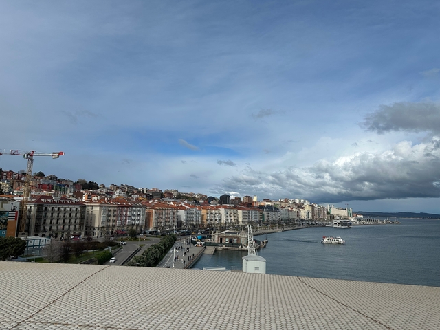 Waterfront cityscape with buildings and cranes.