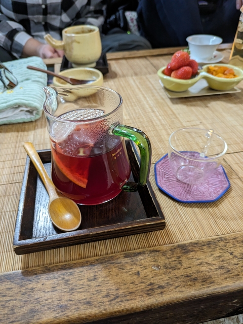 A glass mug of red tea with steam and lemon slice.