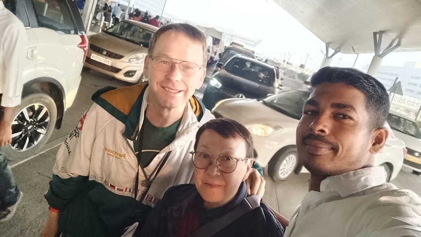 Two people in front of parked cars, at what appears to be an airport or transport terminal