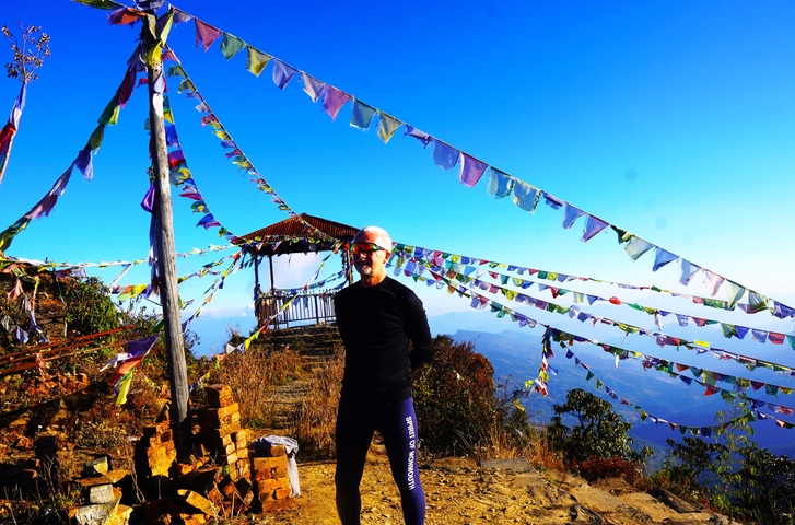 Person standing with prayer flags in the foreground and a mountainous view