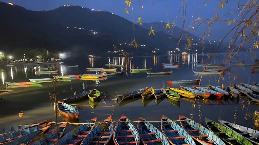       Colorful boats on a lake at night, with reflections.
  