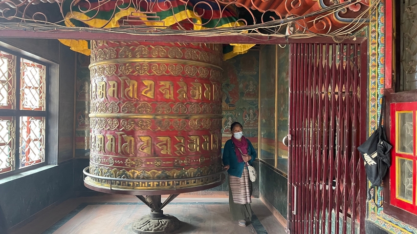       Person standing beside a large prayer wheel.
  