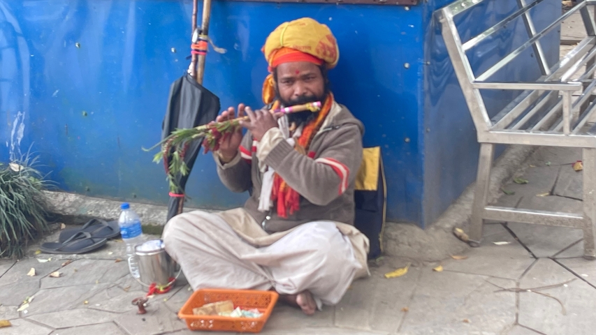       Person playing a flute while sitting on a sidewalk.
  