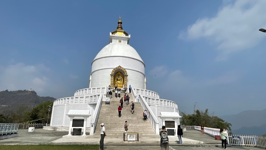       White stupa with visitors and a blue sky.
  