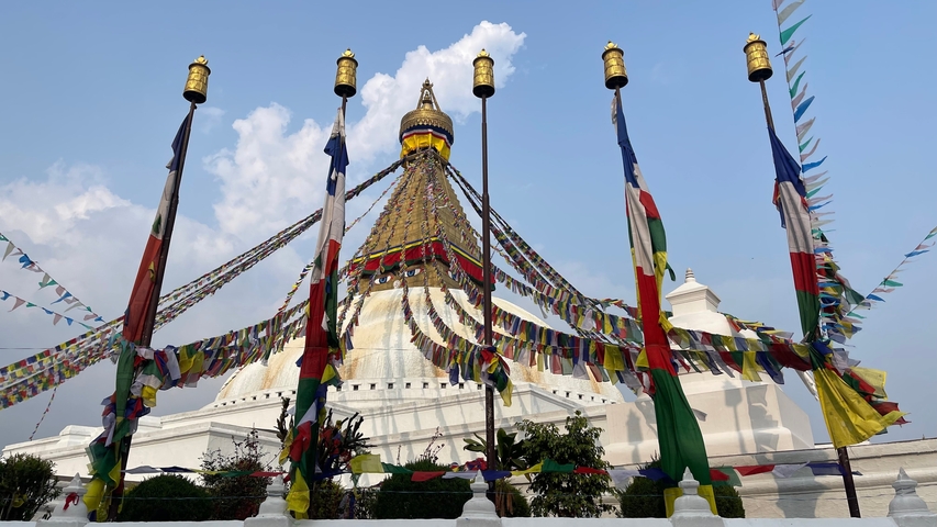       Large stupa with prayer flags under a blue sky.
  