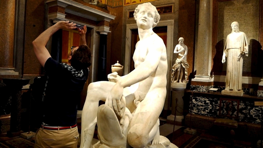       Statue of a seated figure inside a museum gallery.
  